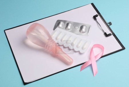 Visita al ginecólogo, Salud de la mujer. Portapapeles, enemas vaginales, píldoras y cinta de conocimiento de cáncer de mama rosa sobre fondo azul.