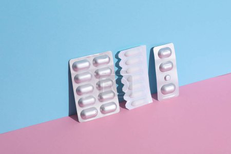 Vaginal suppositories and blisters of pills on a blue-pink background