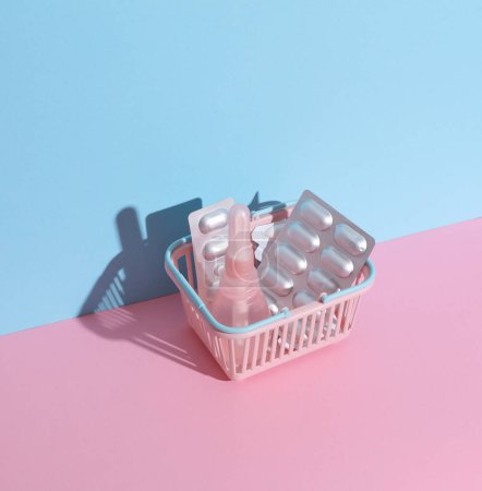 Mini cesta de supermercado con enema vaginal, pastillas sobre fondo rosa azul. Mujeres Salud