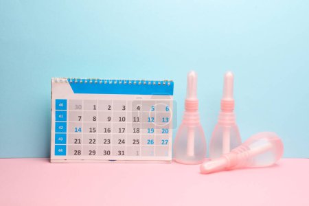 Normalisation du cycle menstruel. Calendrier et lavements vaginaux en fond bleu rose