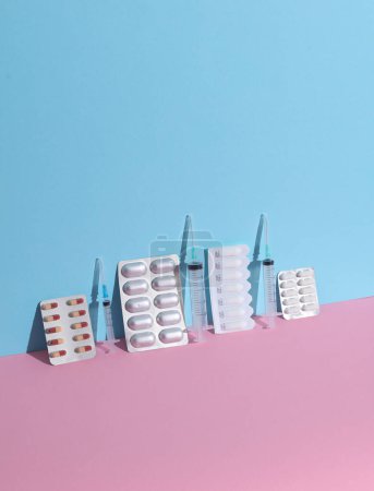 Verschiedene Medikamente, Tablettenblasen mit Spritzen auf blau-rosa Hintergrund. Kreatives Layout, minimalistisches Medizinkonzept