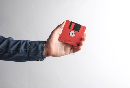 Téléchargez les photos : Main d'homme en chemise denim tenant une disquette rouge sur fond gris - en image libre de droit