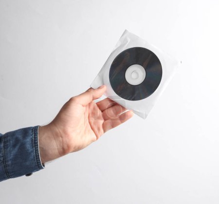 Photo for Man's hand in denim shirt holding CD disk in pack on gray background - Royalty Free Image