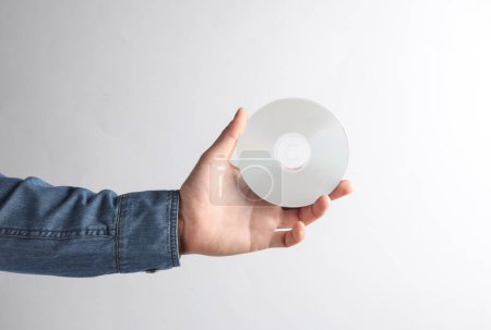 Photo for Man's hand in denim shirt holding white CD disk on gray background - Royalty Free Image