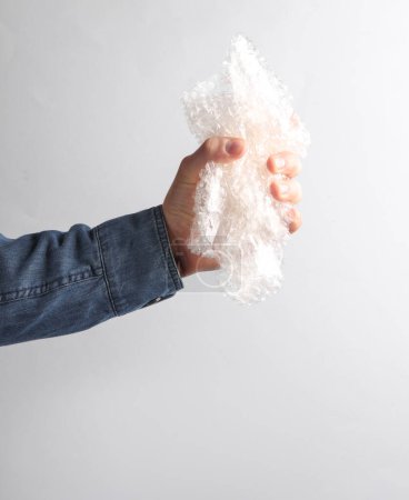 Man's hand in denim shirt holding bubble wrap on gray background