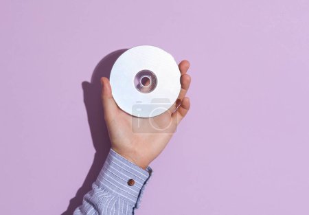 Photo for Man's hand in shirt holding cd disk on purple pastel background with shadow. - Royalty Free Image