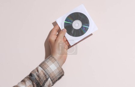Photo for Man's hand in shirt holding cd disk in pack on beige background with shadow - Royalty Free Image