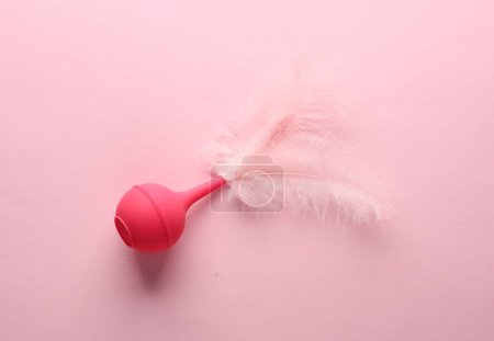 Pink enema with feathers on a pink background. Minimalism