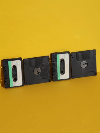 Téléchargez les photos : Des technologies obsolètes. Cassette audio rétro des années 80 et disquettes sur fond jaune avec ombre. Mise en page créative - en image libre de droit