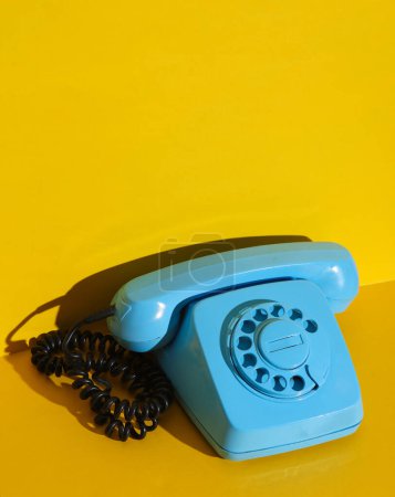 Foto de Teléfono rotativo retro rotatorio pintado en pintura azul sobre un fondo de pared amarillo. Diseño creativo - Imagen libre de derechos