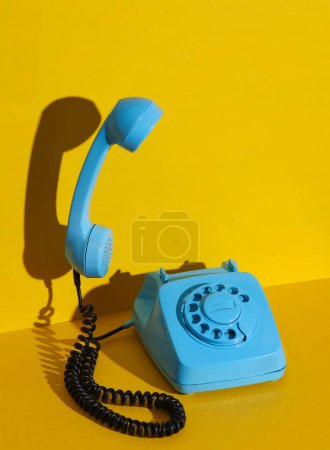 Téléchargez les photos : Téléphone rotatif rétro rotatif avec un combiné flottant peint en peinture bleue sur un fond jaune avec ombre. Mise en page créative - en image libre de droit