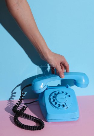 Téléchargez les photos : HAnd tenant bleu téléphone rotatif rétro rotatif combiné sur fond bleu rose avec ombre. Mise en page créative - en image libre de droit