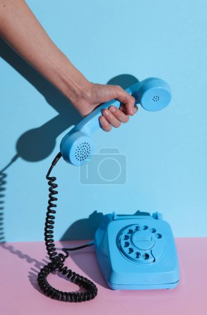 Foto de HAnd sostiene el teléfono retro giratorio azul giratorio sobre fondo azul rosado con sombra. Diseño creativo - Imagen libre de derechos