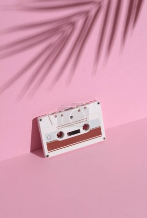 Retro 80s audio cassette on a pink background with palm leaf shadow. Creative layout, minimalism