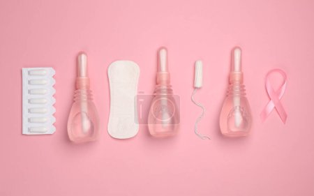Women's health concept. Vaginal enemas, pad, tampon and pink awareness ribbon on pink background. Flat lay
