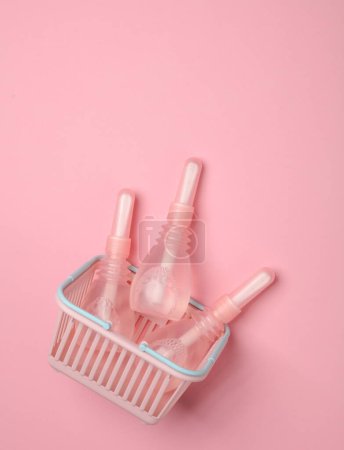 Cesta de supermercado con tres enemas vaginales sobre fondo rosa. Salud de la mujer