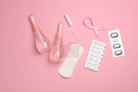 Women's health concept. Vaginal enemas, pad, tampon, pills and pink awareness ribbon on pink background. Flat lay