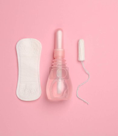 Women's health concept. Vaginal enema, pad, tampon on pink background. Flat lay