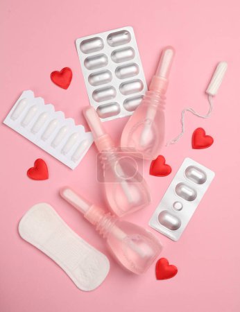 Women's health concept. Vaginal enemas, pad, tampon, pills and hearts on pink background. Flat lay