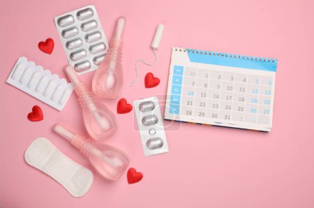 Women's health concept. Calendar, Vaginal enemas, pad, tampon, pills and hearts on pink background. Menstruation cycle. Flat lay