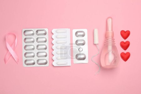 Women's health, treatment of women's diseases. Vaginal suppositories, pill blisters, tampon, pink awareness ribbon on pink background. Flat lay