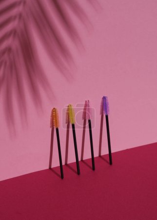 Téléchargez les photos : Set de pinceaux pour peigner les cils sur fond rose avec ombre à feuilles de palmier. Concept de beauté - en image libre de droit