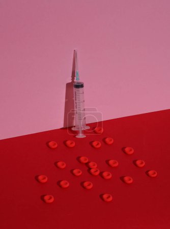 Spritze und rote Blutkörperchen auf farbigem Hintergrund. Medizinkonzept. Kreative Gestaltung