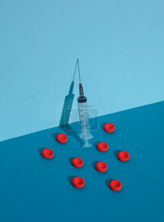 Syringe and Red blood cells on blue background. Medicine concept. Creative layout