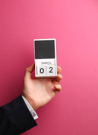 2 de marzo calendario de bloques de madera en mano masculina sobre fondo rosa
