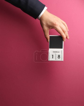 18 de marzo calendario de bloques de madera en mano masculina sobre fondo rosa