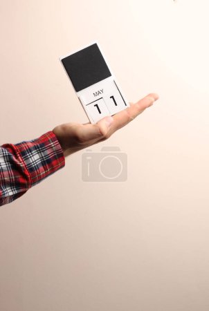 Fecha 11 de mayo, calendario de bloques en mano masculina sobre fondo beige