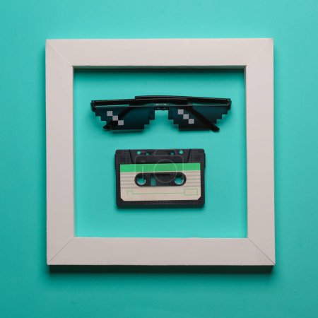 Pixel sunglasses and audio cassette in white frame on blue background. Creative layout. Minimalism