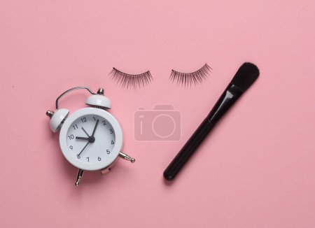 Foto de Falsas pestañas y cepillo de maquillaje, despertador sobre fondo rosa. Concepto de belleza - Imagen libre de derechos