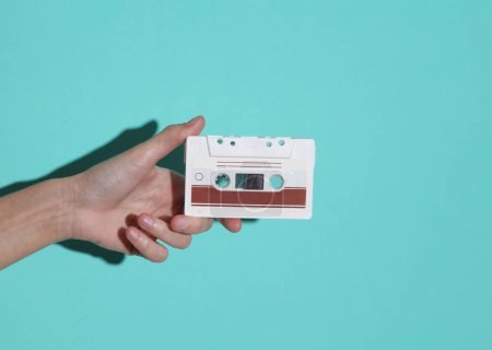 Weibliche Hand mit Retro-80er-Audio-Kassette auf blauem Hintergrund mit Schatten