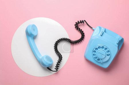 Retro blue painted rotary phone on a pink background with a white circle. Top view. Minimalism