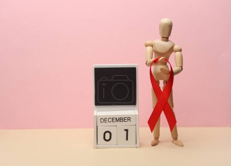 Holzpuppe mit rotem Band und Kalender mit Datum 1. Dezember auf rosa Hintergrund. Welttag gegen HIV-Aids 