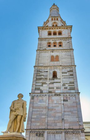 Photo for Modena, Italy - March 5, 2019: Upward view of the Ghirlandina tower with the monument of the poet Alessandro Tassoni - Royalty Free Image