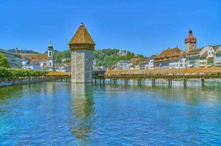 Foto de Lucerna, Suiza - 13 de julio de 2022: El puente cubierto de madera de la capilla con la torre octogonal de agua en el río Reuss, en el fondo del casco antiguo - Imagen libre de derechos