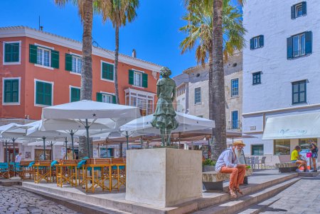 Téléchargez les photos : Mahon / Minorque, Espagne - 4 août 2022 : Touristes sur la place Colon avec la statue d'une jeune femme (les versets du poète Pilar Alonso et le nom de la fondation qui a donné la statue sont gravés sur la base) - en image libre de droit