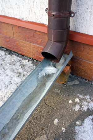 Foto de Plastic brown downspout with frozen rainwater in winter. Roof drain pipe. Waterspout. Water roofing rain pipeline. Selective focus. - Imagen libre de derechos