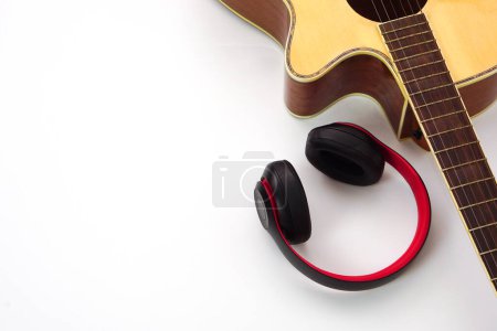 Acoustic guitar on a white background and the headphones are placed on the side. Concept of love, leisure and music.