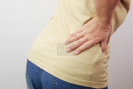 Téléchargez les photos : Woman hands touching her buttocks area suffering from pain. Health care and medical concept. - en image libre de droit