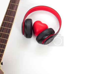 Guitarra acústica, auriculares y corazón rojo sobre fondo blanco. Amor, entretenimiento y concepto musical.
