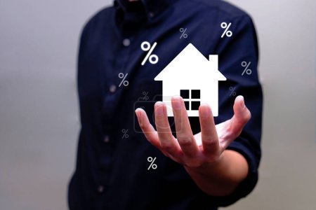 Téléchargez les photos : Main de l'homme tenant la maison virtuelle avec des pourcentages autour d'elle. Financement des taux d'intérêt, immobilier et concept de prêt immobilier. - en image libre de droit