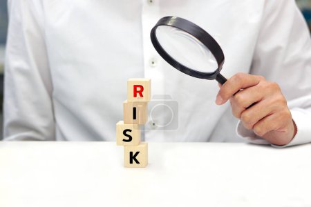 Hand eines Geschäftsmannes, der eine Glaslupe über den Holzklötzen mit dem Schriftzug RISK hält. Konzept der Risikoanalyse, Unternehmensführung und Strategie.