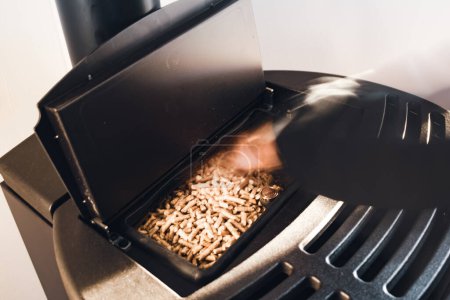 Photo for Pellet stove, man spreading pellets in a modern black stove - Royalty Free Image