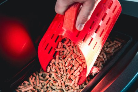 Close-up on pellets, black domestic pellet stove, man loading by hand granules with a red 3 d printed cup