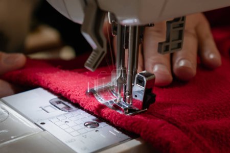 Foto de Hombre usando una máquina de coser con una prenda roja, para trabajos de reparación, personalización, creación, upcycling - Imagen libre de derechos