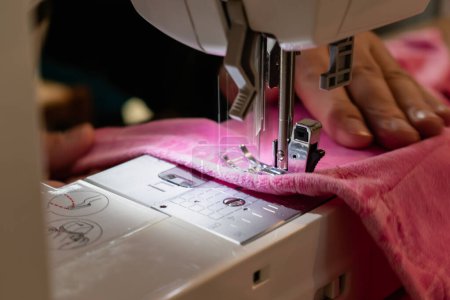 Foto de Hombre usando una máquina de coser con una prenda rosa, para trabajos de reparación, personalización, creación, upcycling - Imagen libre de derechos