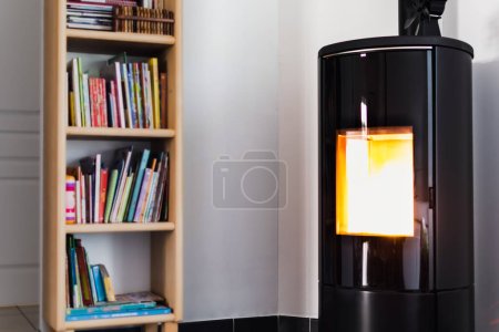 Photo for Pellet stove burning with flame in a living room with bookcase and heat diffuser - Royalty Free Image